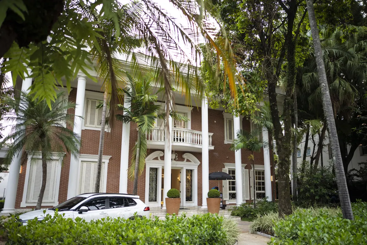 Fachada do Núcleo GA, mansão com colunas brancas entre palmeiras